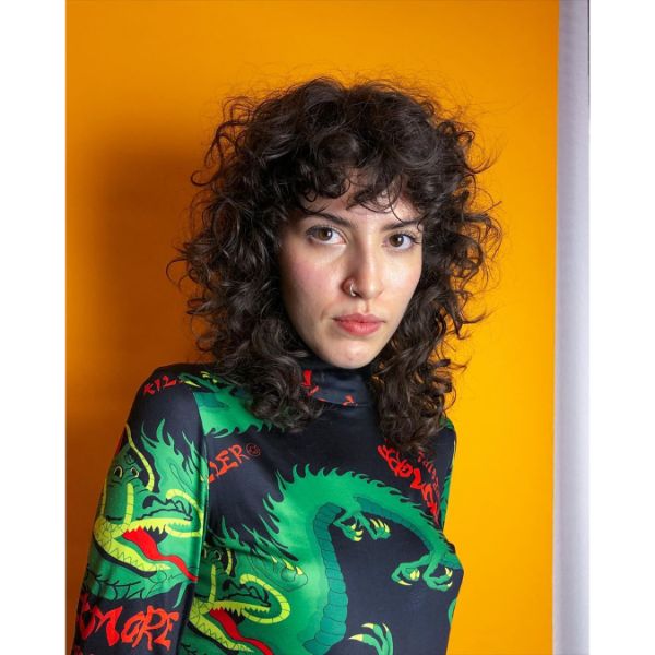 Long Curly Shag Haircuts for Women with Curly Bangs - a woman with a dragon blouse