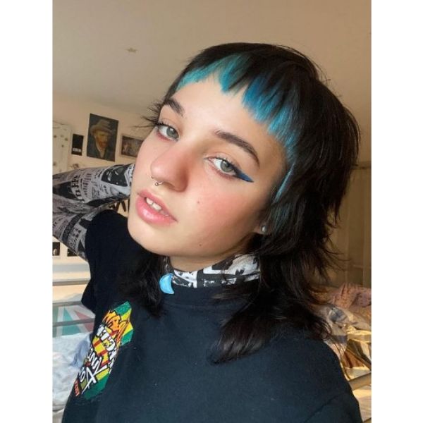 A girl indoor with her short dark mullet with blue bangs hairstyle