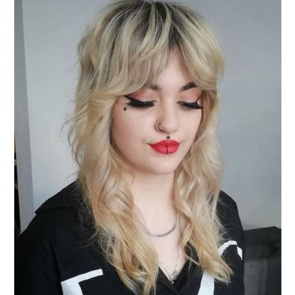 A girl with make up with her long wavy blonde shag with dark roots hairstyle