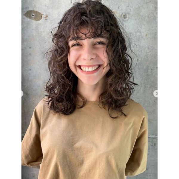 A girl smiling with her shaggy perm with curly bangs haisrtyle