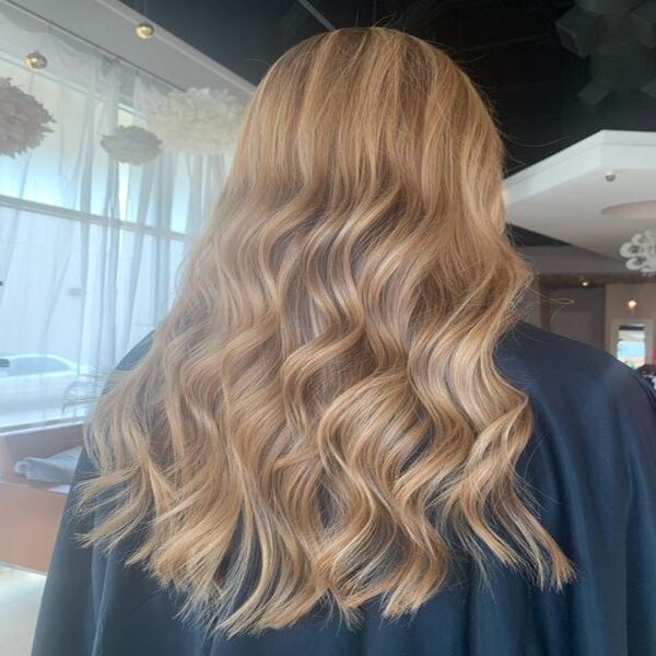 Golden Caramel Balayage for Curly Long Hair- A women inside a salon
