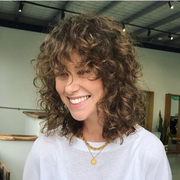 curly wolf cut for curly hair - a smiling woman wearing a necklace and a white shirt