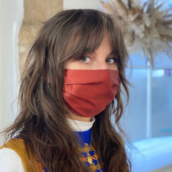 a white woman wearing a mustard facemask have her hair styled into layered wolf cut for thick hair