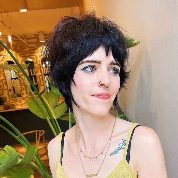 short wolf cut with bangs - a woman with a flower tattoo and is wearing a gold necklace