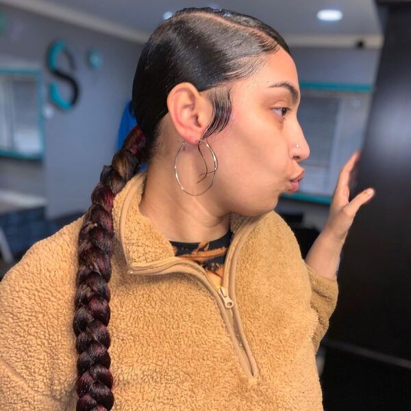 Low Sleek Braided Ponytail with Baby Hair - A woman with earrings wearing a brown coat jacket