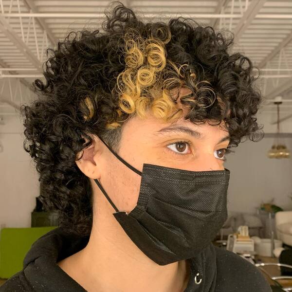 Curly Mullet With Sunflower Blonde Highlights - a woman wearing a black face mask