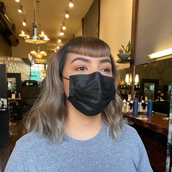 Icy Blonde and Curved Blunt Bangs - a woman wearing a face mask