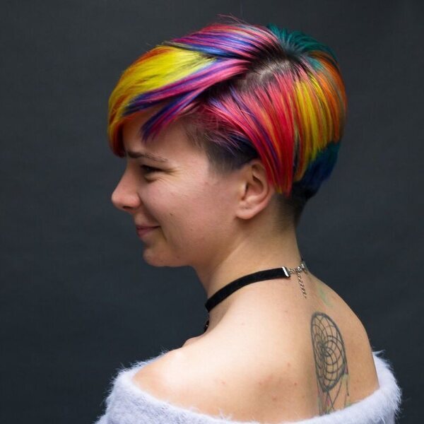 Short Bob Cut Rainbow Hair Color - A woman with a tattoo wearing a white off shoulder coat