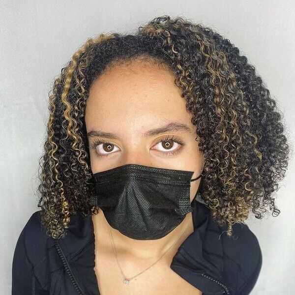 Poppin Curls with Honey Blonde Highlights - a woman wearing a black face mask